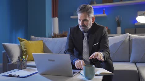 Businessman-working-on-laptop-alone-in-living-room-at-night-at-home.
